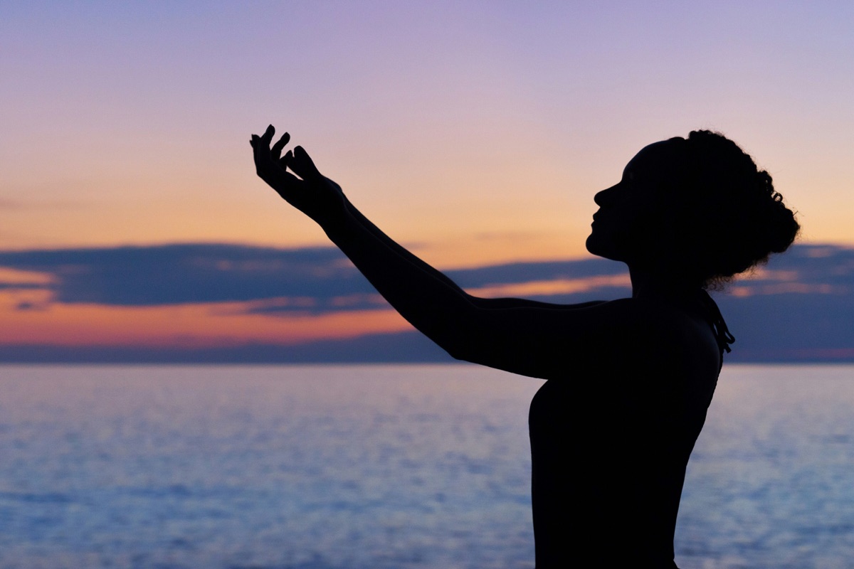 A silhouette reaching toward the horizon at sunset, evoking inner peace